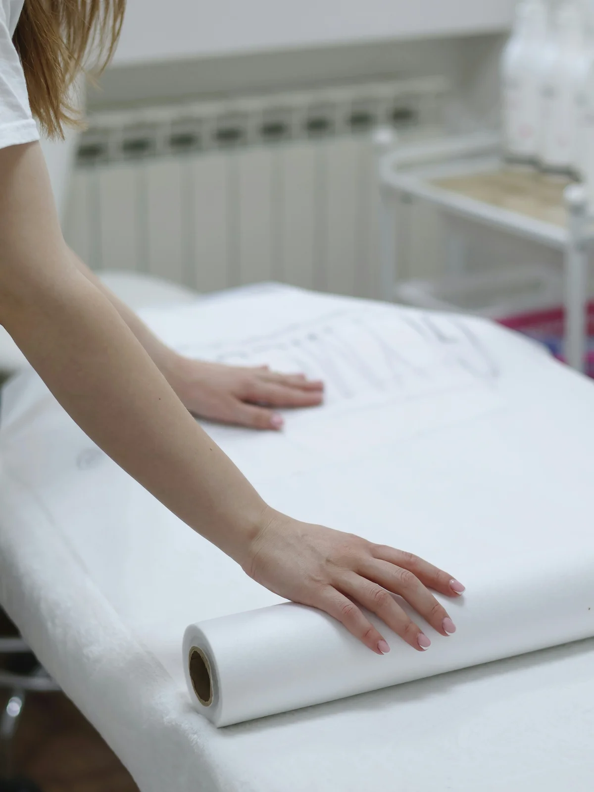 Grande plano dos braços de uma esteticista a desenrolar uma folha de papel limpa sobre uma marquesa para preparar um tratamento