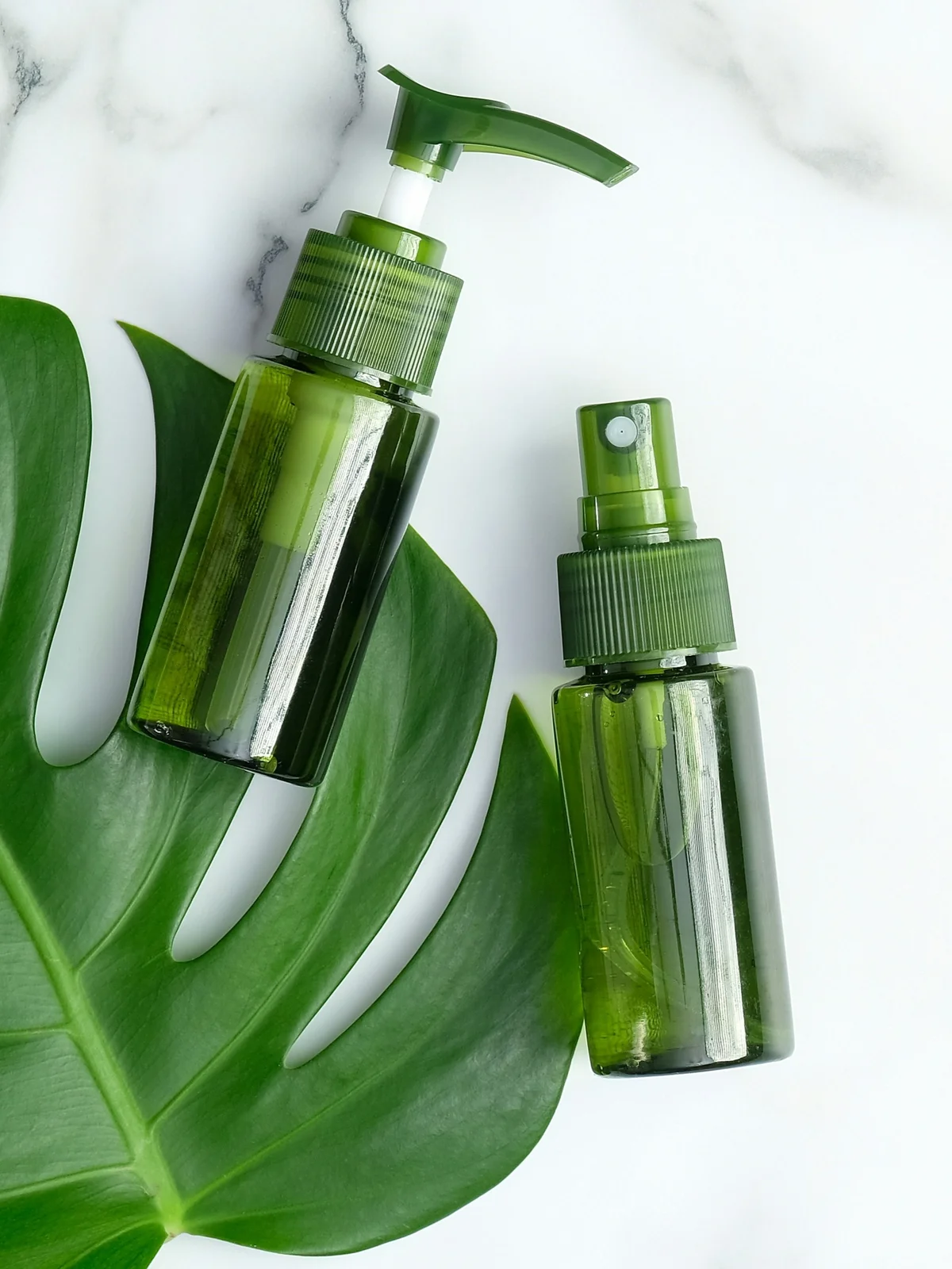 Composição plana com dois frascos verdes de géis e séruns refrescantes sobre uma folha verde e uma superfície de mármore branco