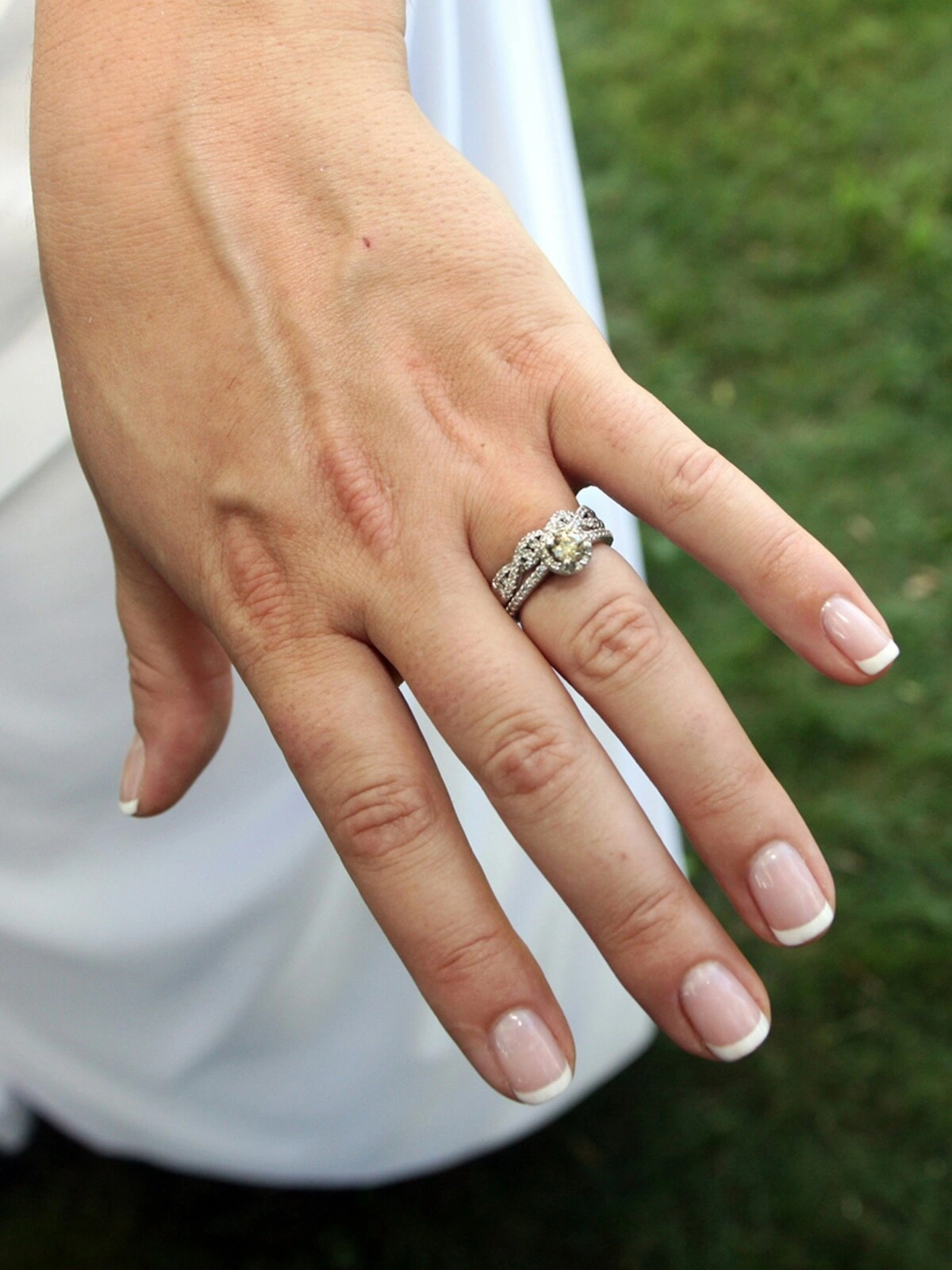 A mão de uma mulher com uma manicure francesa cuidada numa combinação clássica de nude e branco em unhas curtas de formato quadrado-oval