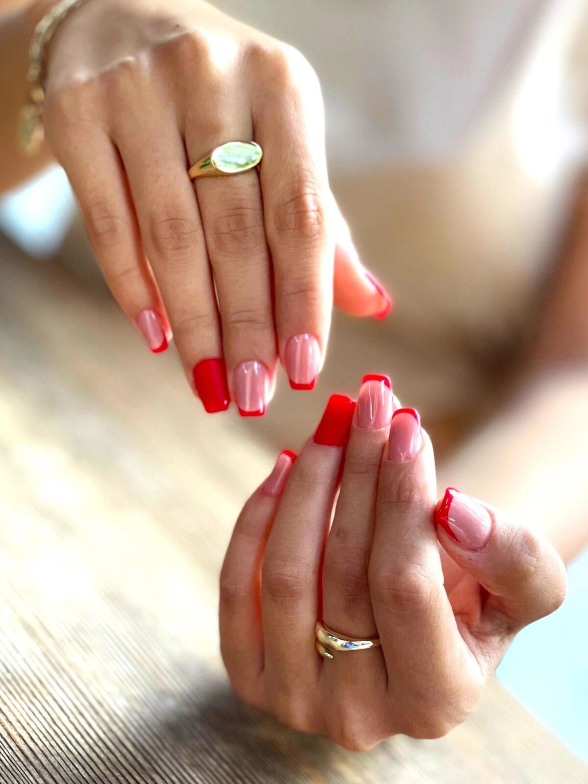 Uma manicure francesa em unhas quadradas-ovais com base rosa-claro e pontas vermelhas, e os dedos anelares totalmente em vermelho