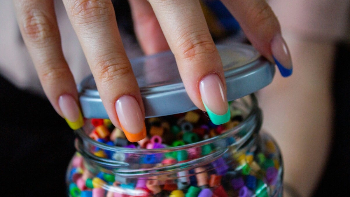A mão de uma mulher com uma manicure francesa de base nude transparente e pontas multicoloridas
