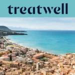 Vista ampla sobre uma cidade costeira siciliana, com edifícios antigos de telhados em terracota, uma meia-lua de praia de areia, um mar turquesa cristalino e um promontório rochoso que se ergue de um dos lados.