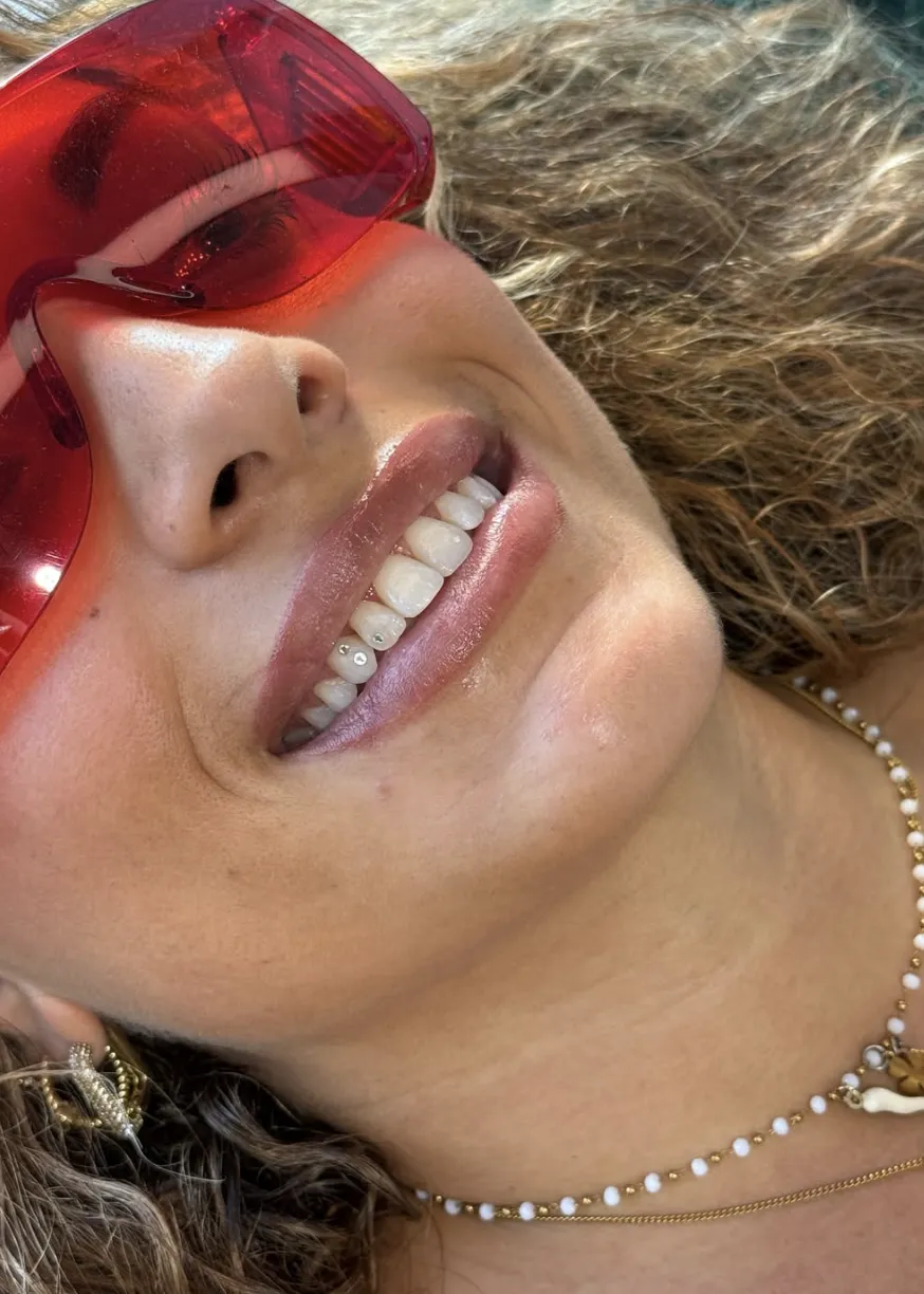 Grande plano de um sorriso com dois pequenos piercings dentários de cristal nos dentes inferiores, retrato de verão